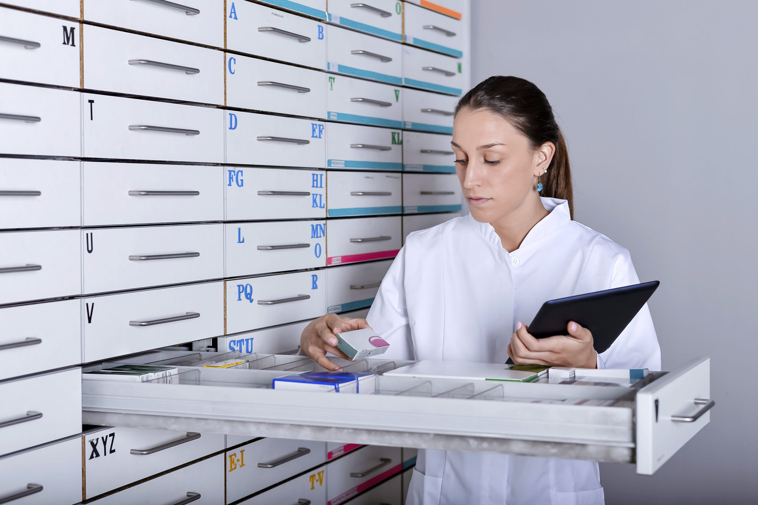 Young pharmacist standing next to medicine shelves, holding tablet